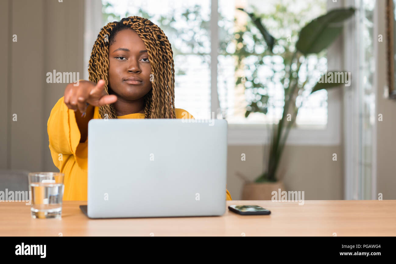 African american woman with laptop pointing with finger to the camera ...