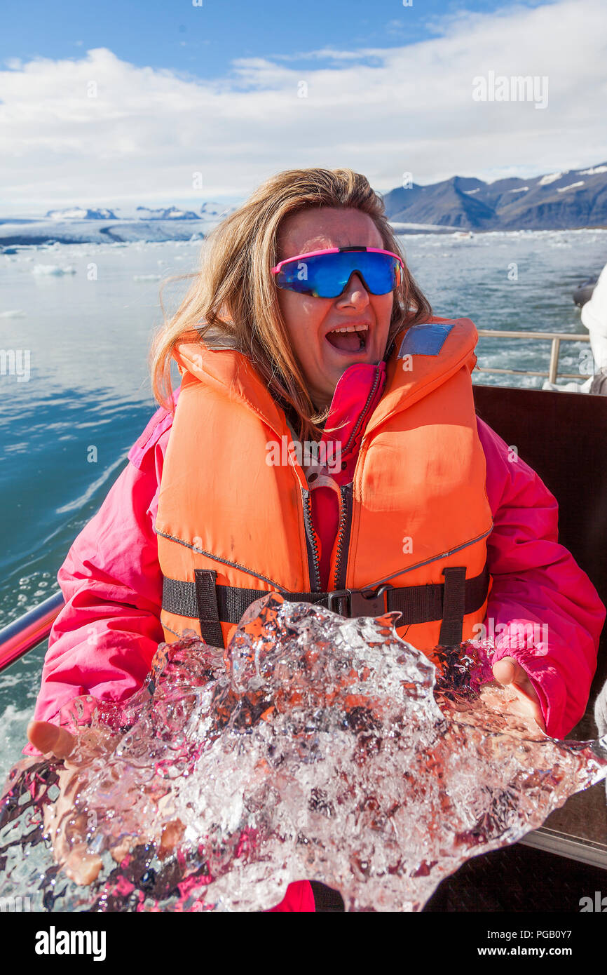 beautiful mature woman having fun raising a piece of iceberg on the boat in the lagoon of Jokulsarlon Stock Photo