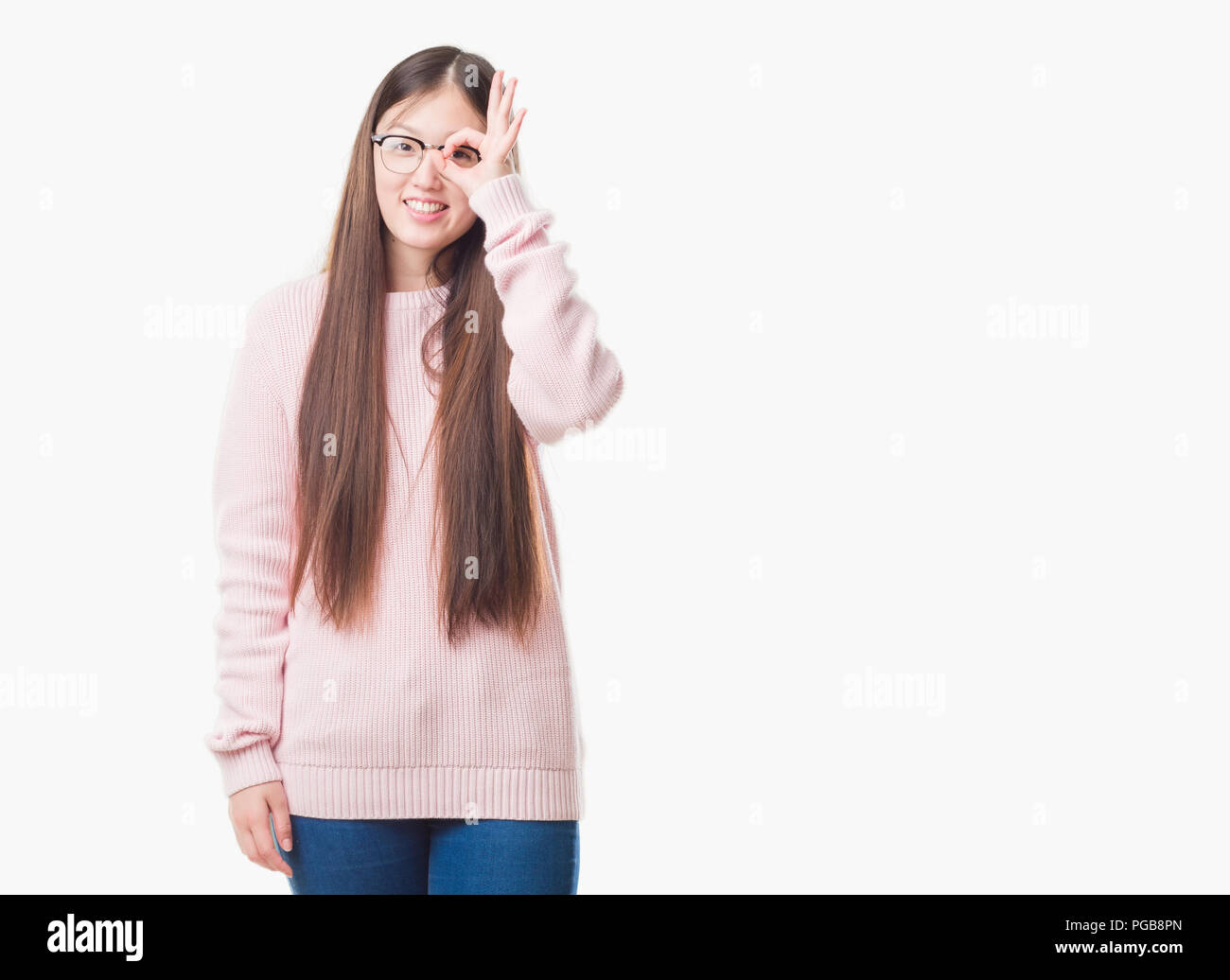 Young Chinese woman over isolated background wearing glasses doing ok gesture with hand smiling, eye looking through fingers with happy face. Stock Photo