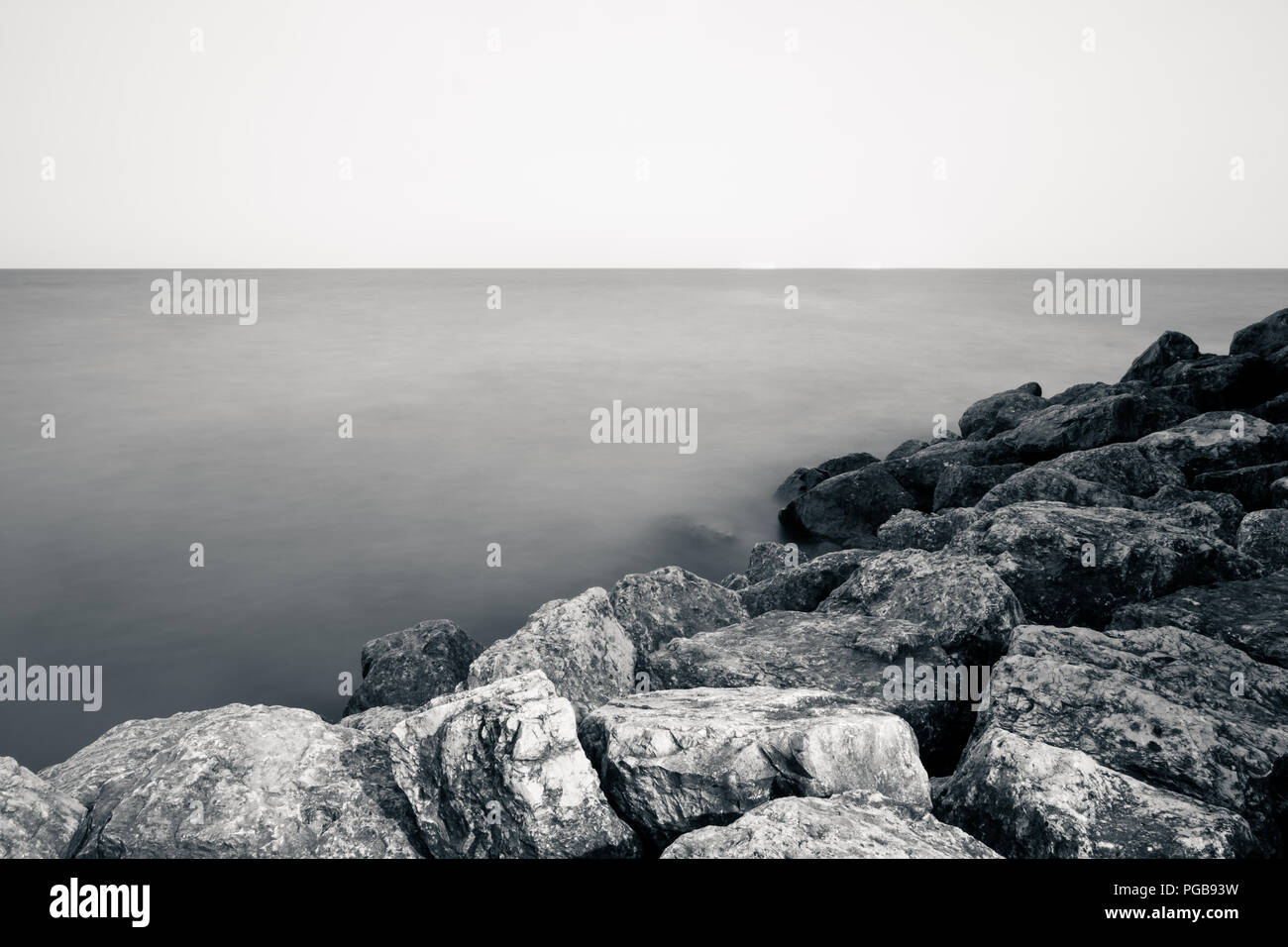 Long-exposure photograph of a smooth, peaceful lake beside a rocky coastline. Stock Photo