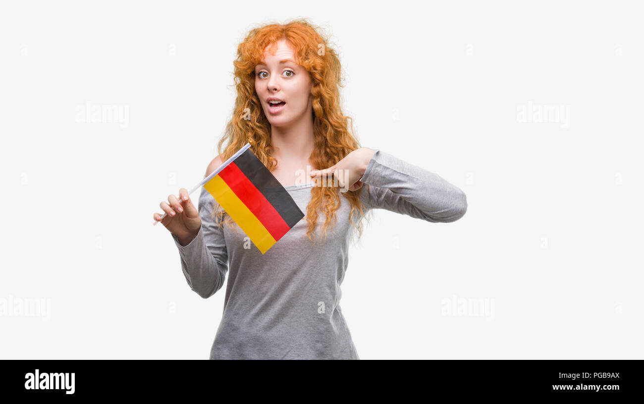 Young Redhead Woman Holding Flag Of Germany With Surprise Face Pointing Finger To Himself Stock Young Redhead Woman Holding Flag Of Germany With Surprise Face Pointing Finger To Himself Stock
