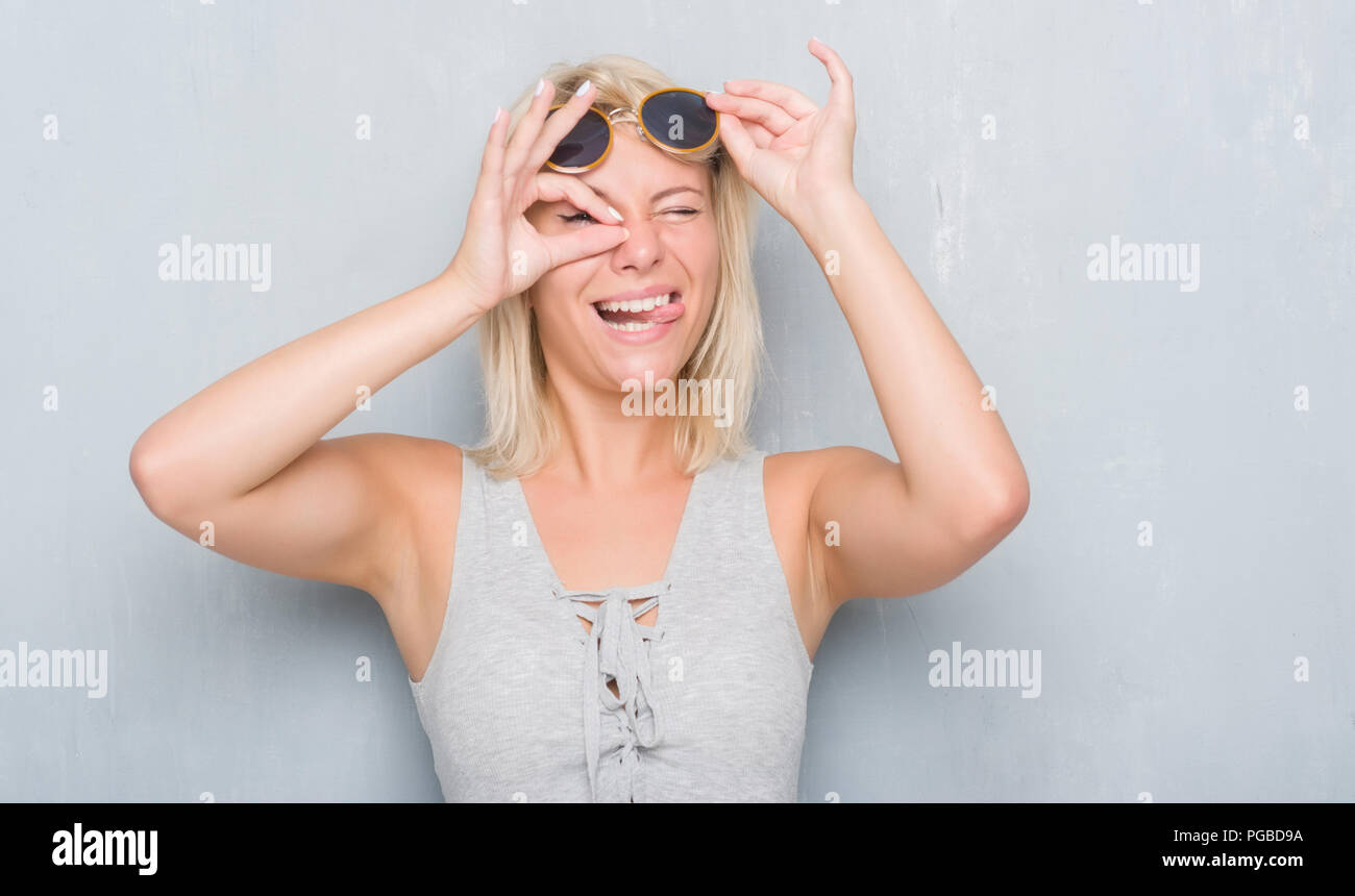 Adult caucasian woman over grunge grey wall wearing retro sunglasses ...