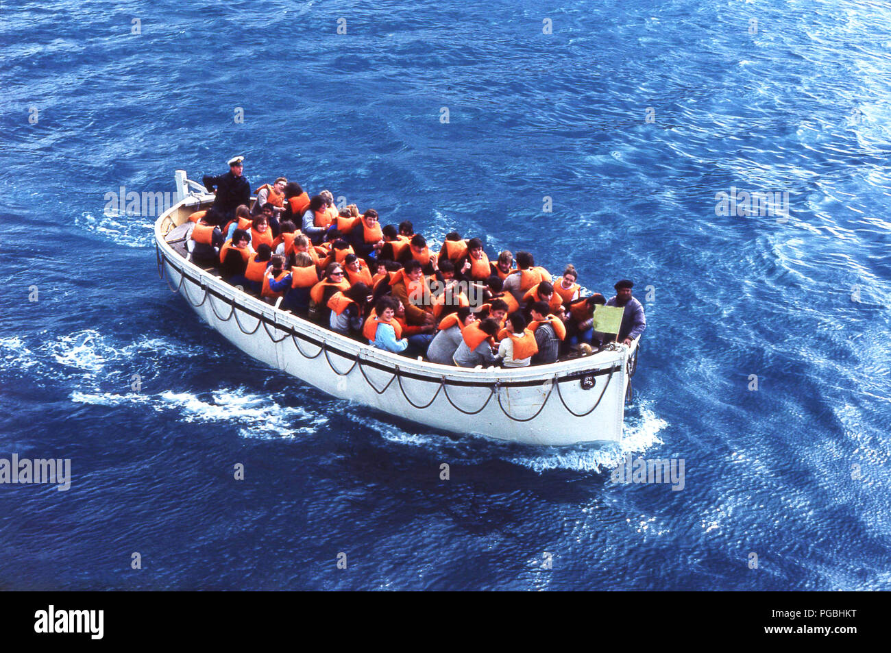 1970s, historical, cruise passengers with orange coloured life jackets, out at sea on a lifeboat taking part in a ship's life safety drill. Stock Photo
