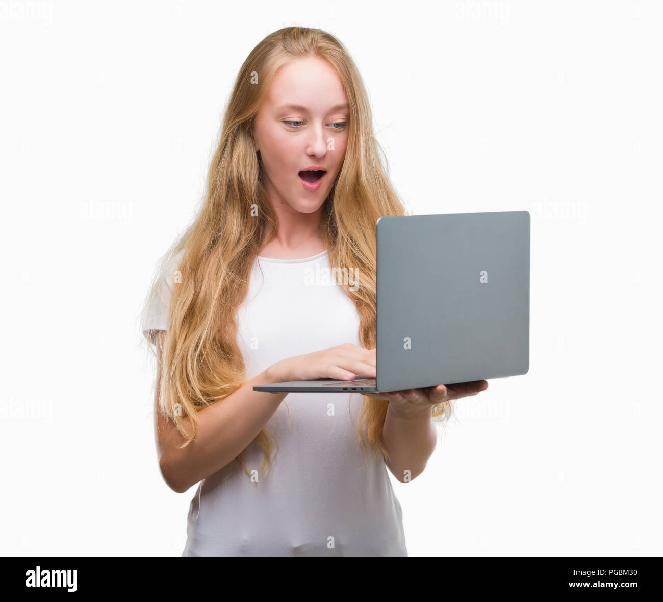 Blonde teenager woman using computer laptop scared in shock with a ...