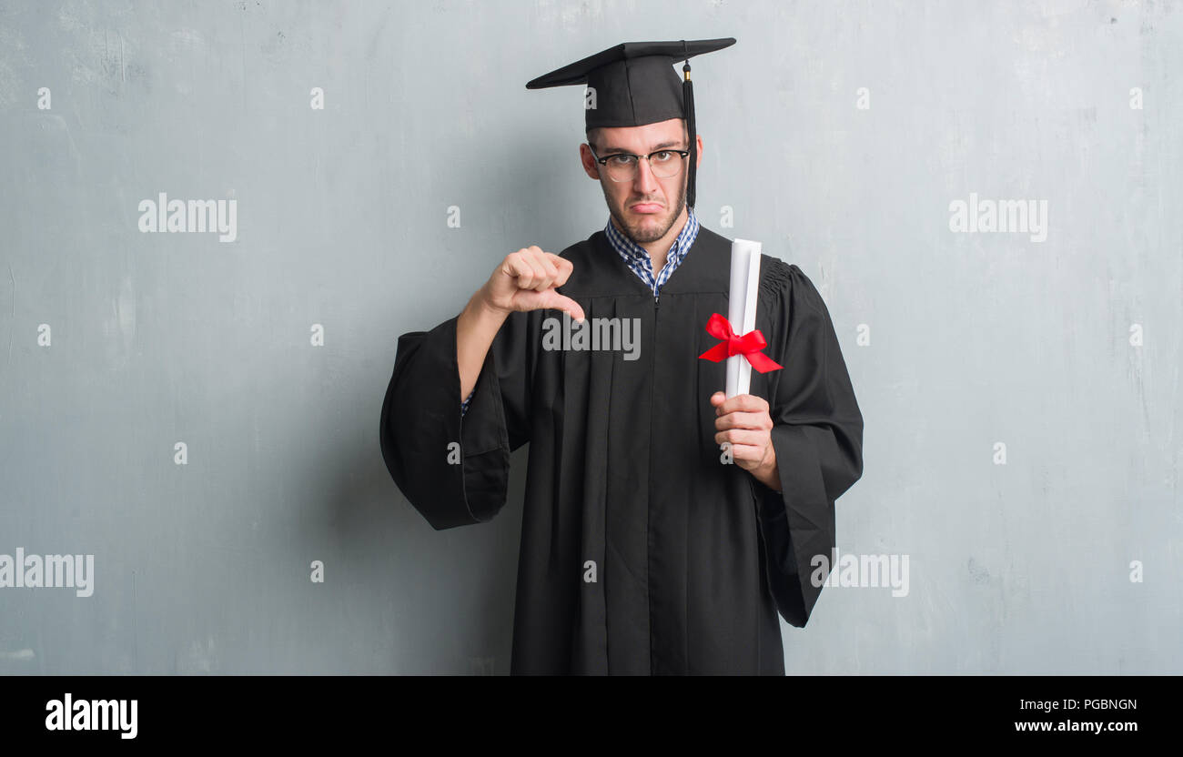 Young caucasian man over grey grunge wall wearing graduate uniform ...
