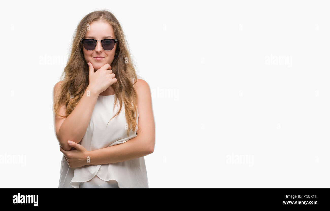 Young blonde woman wearing sunglasses looking confident at the camera with smile with crossed arms and hand raised on chin. Thinking positive. Stock Photo