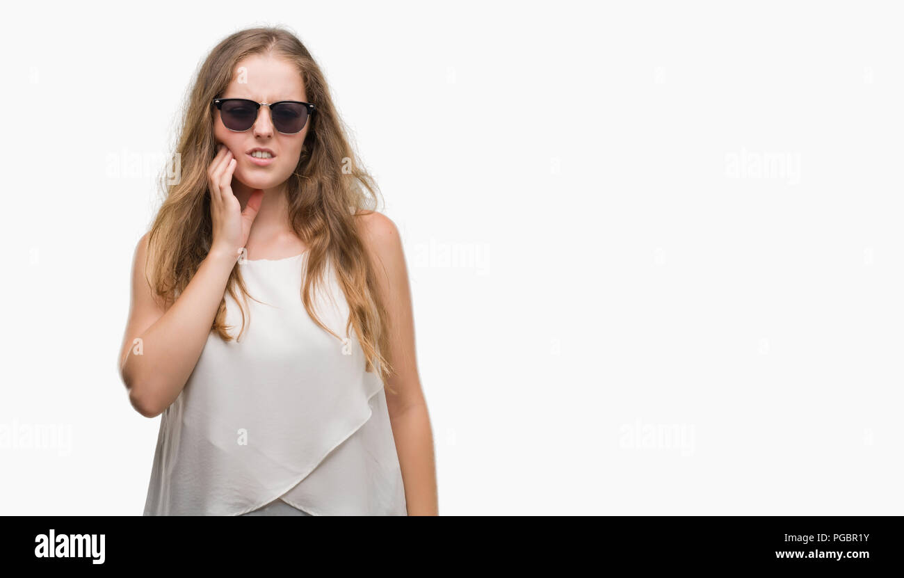 Young blonde woman wearing sunglasses touching mouth with hand with painful expression because of toothache or dental illness on teeth. Dentist concep Stock Photo
