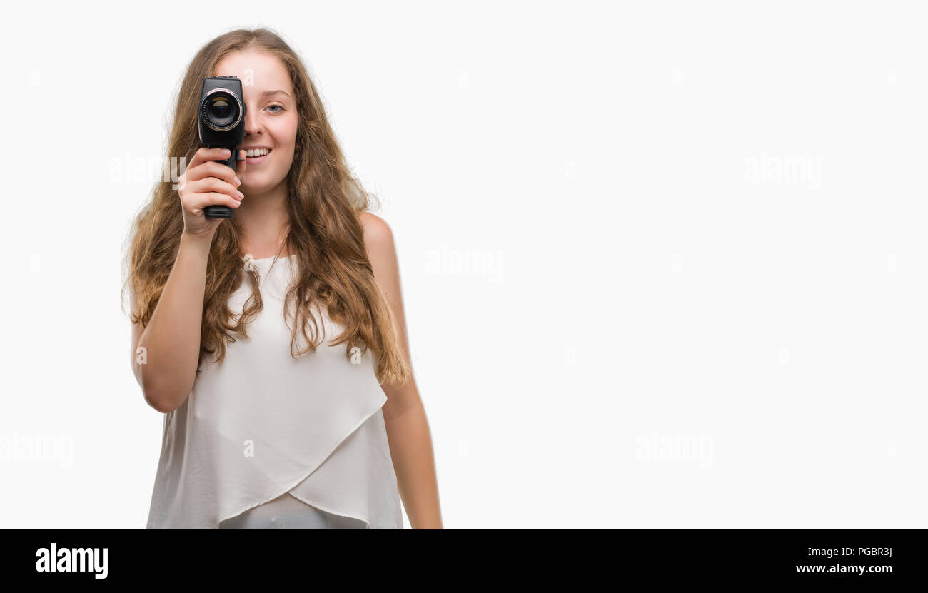 Young blonde woman holding super 8 video camera with a happy face standing and smiling with a confident smile showing teeth Stock Photo