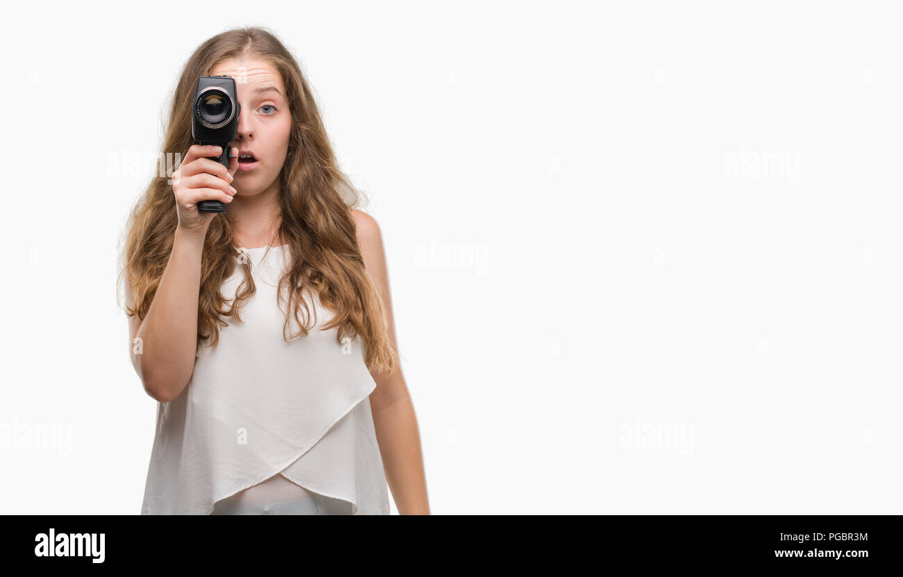 Young blonde woman holding super 8 video camera scared in shock with a surprise face, afraid and excited with fear expression Stock Photo