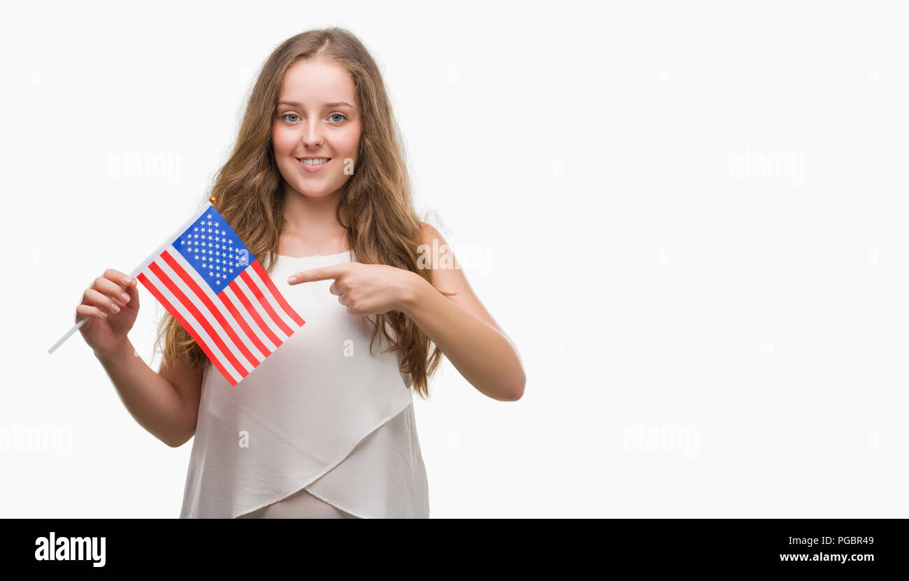Young blonde woman holding flag of USA very happy pointing with hand and finger Stock Photo