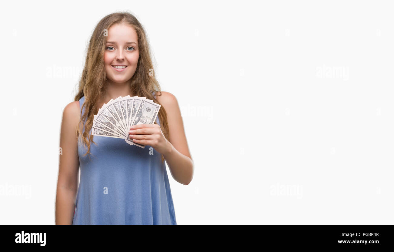 Young blonde woman holding dollars with a happy face standing and smiling with a confident smile showing teeth Stock Photo