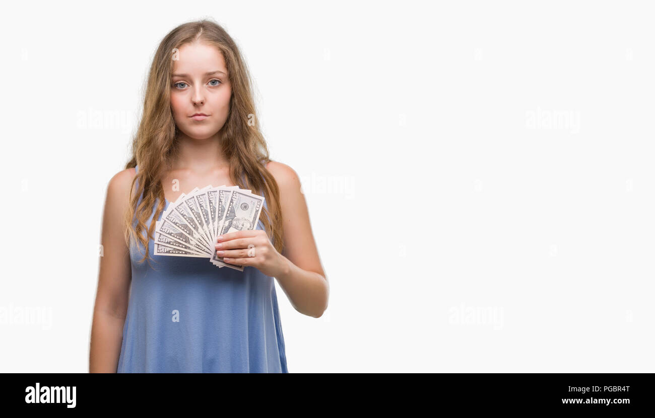 Young blonde woman holding dollars with a confident expression on smart face thinking serious Stock Photo