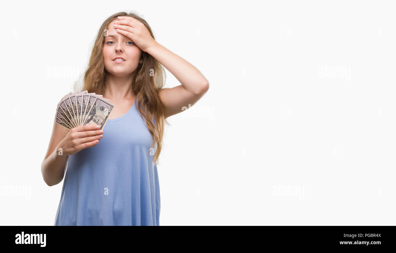 Young blonde woman holding dollars stressed with hand on head, shocked with shame and surprise face, angry and frustrated. Fear and upset for mistake. Stock Photo