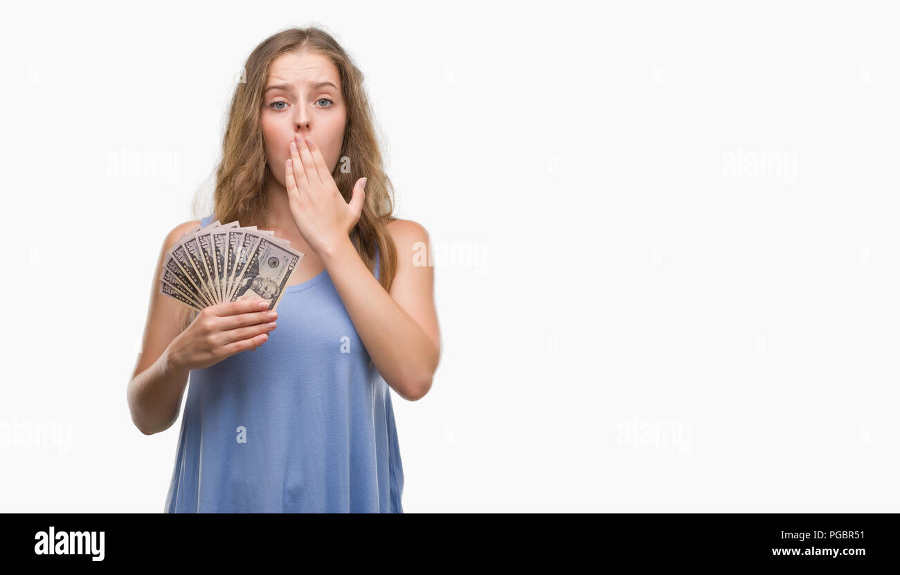 Young blonde woman holding dollars cover mouth with hand shocked with shame for mistake, expression of fear, scared in silence, secret concept Stock Photo