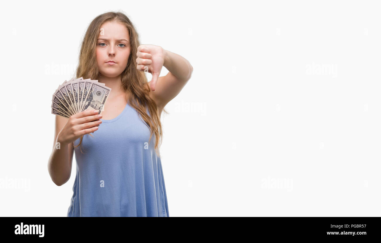 Young blonde woman holding dollars with angry face, negative sign showing dislike with thumbs down, rejection concept Stock Photo