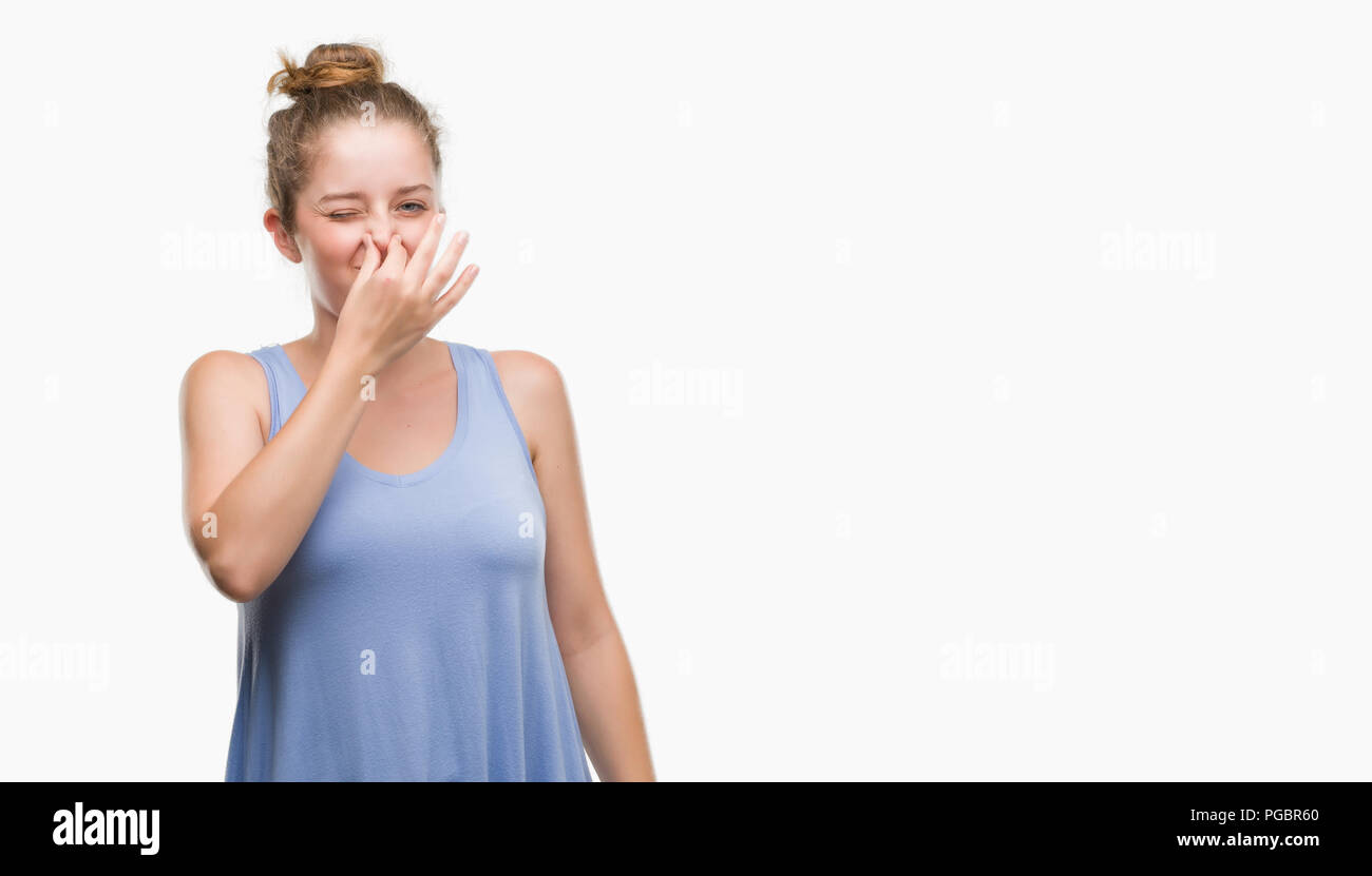 Young blonde woman smelling something stinky and disgusting, intolerable smell, holding breath with fingers on nose. Bad smells concept. Stock Photo