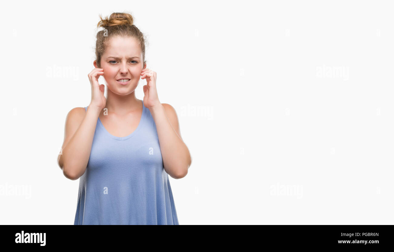 Young blonde woman covering ears with fingers with annoyed expression for the noise of loud music. Deaf concept. Stock Photo