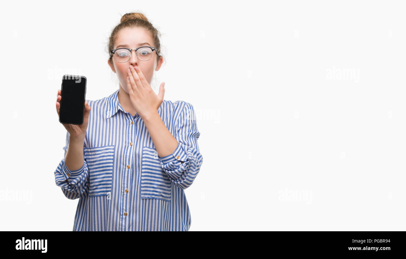 Young blonde woman using smartphone cover mouth with hand shocked with shame for mistake, expression of fear, scared in silence, secret concept Stock Photo