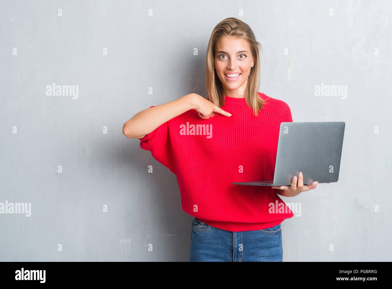 Beautiful young woman over grunge grey wall using computer laptop with ...