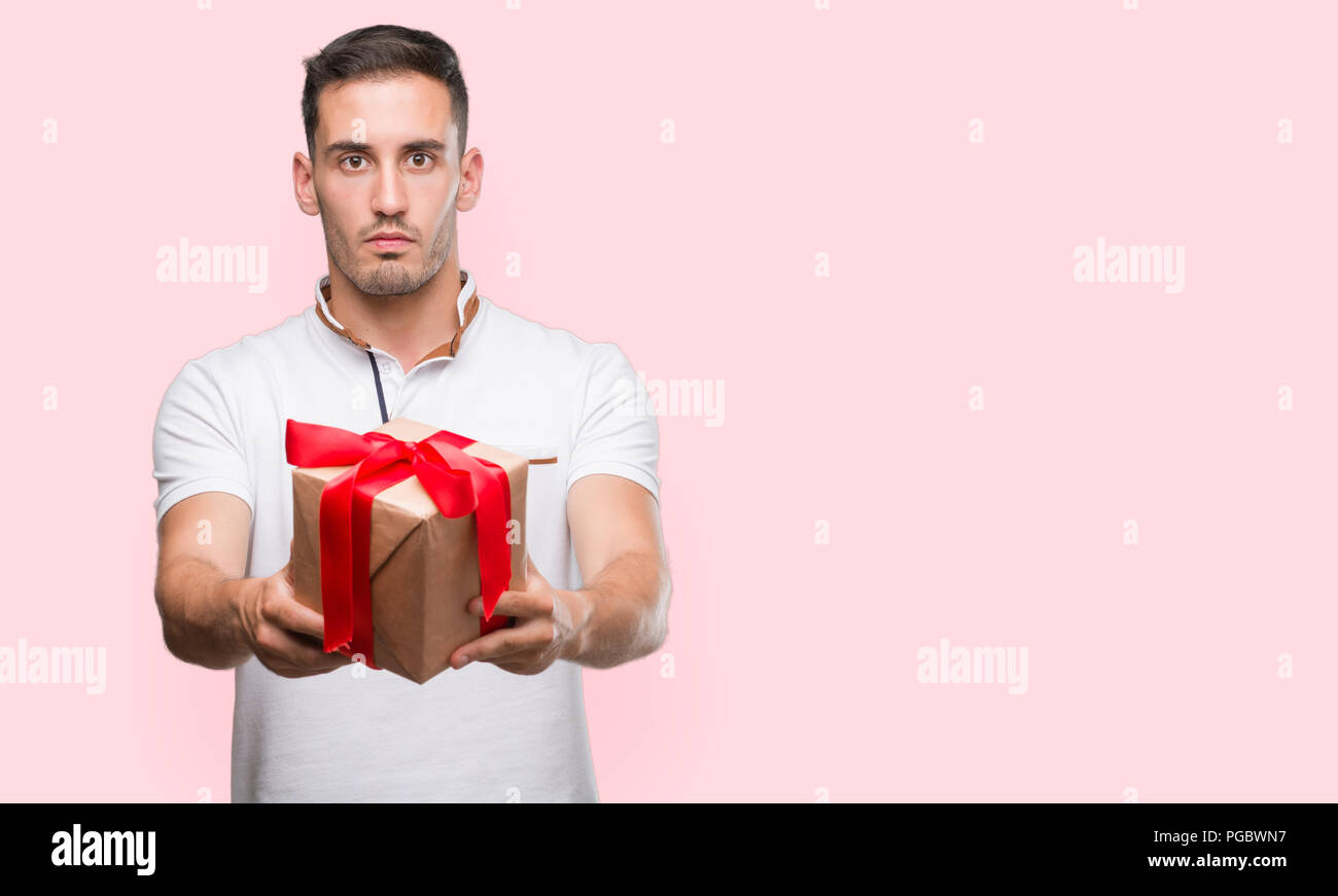 Handsome young man giving a present with a confident expression on ...