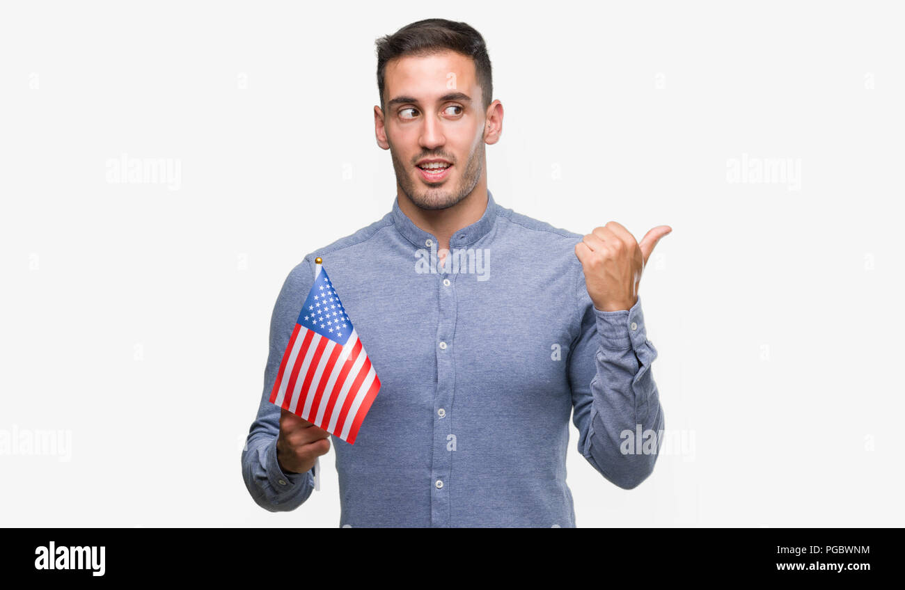 Handsome young man holding a flag of America pointing with hand and ...