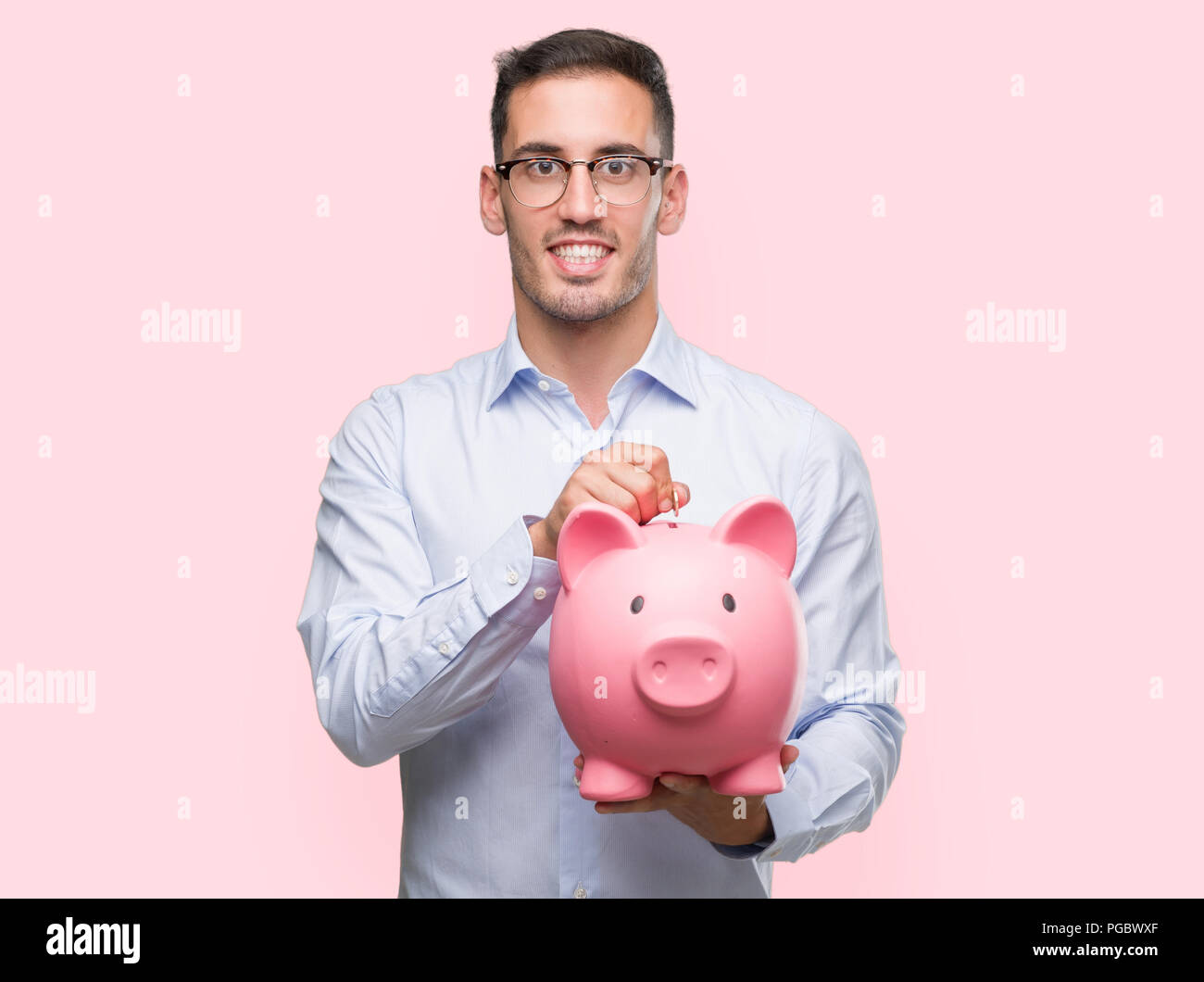 Handsome young man holding a piggy bank with a happy face standing and ...