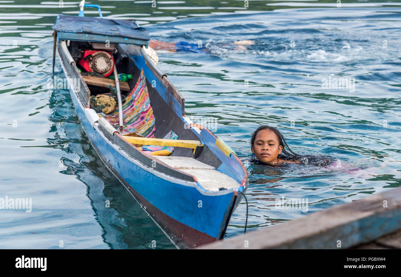 INDONESIA, TOGEAN ISLANDS -MALENGE - JULI 11, 2018: A girl swimming beside traditional wooden boat by  bajo village in Central Sulawesi Stock Photo