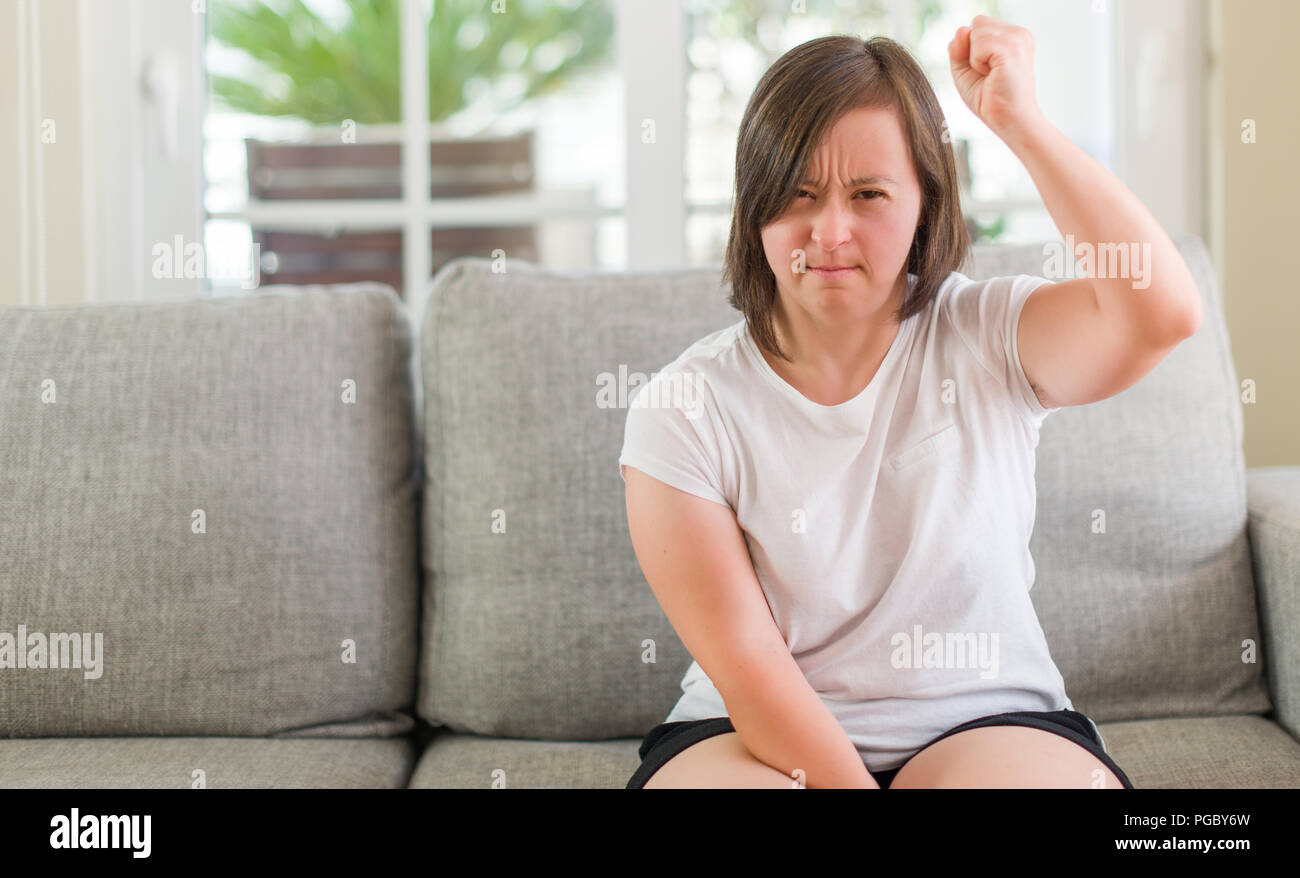Down syndrome woman sitting on the sofa at home annoyed and frustrated shouting with anger, crazy and yelling with raised hand, anger concept Stock Photo