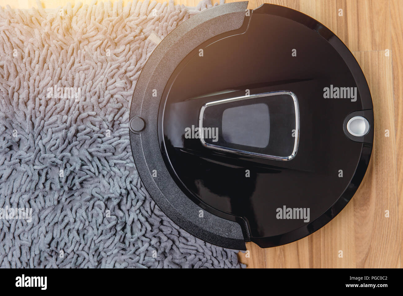 Automate Robot vacuum cleaner on laminate wood floor with carpet cleaning machine. Stock Photo