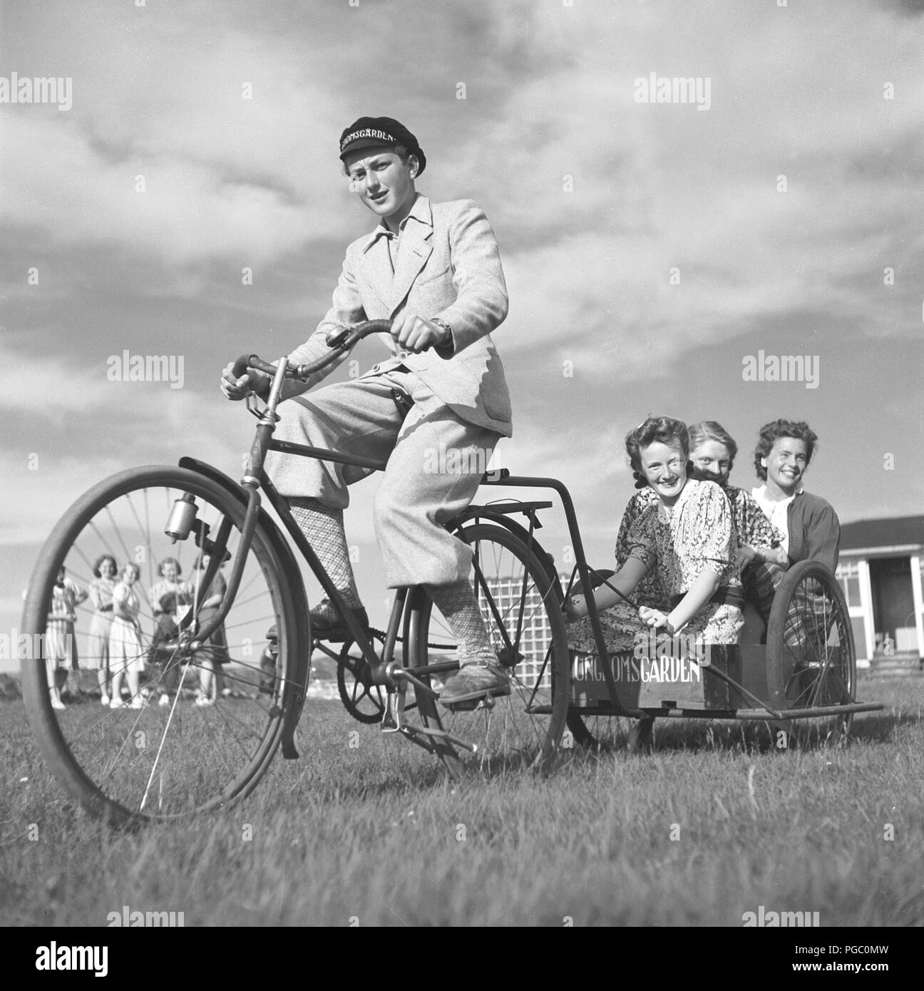 1940s bicycle. A teenage boy on his bicycle is pulling a cart behind with three happily smiling girls. Sweden 1944. Photo Kristoffersson H12-3 Stock Photo