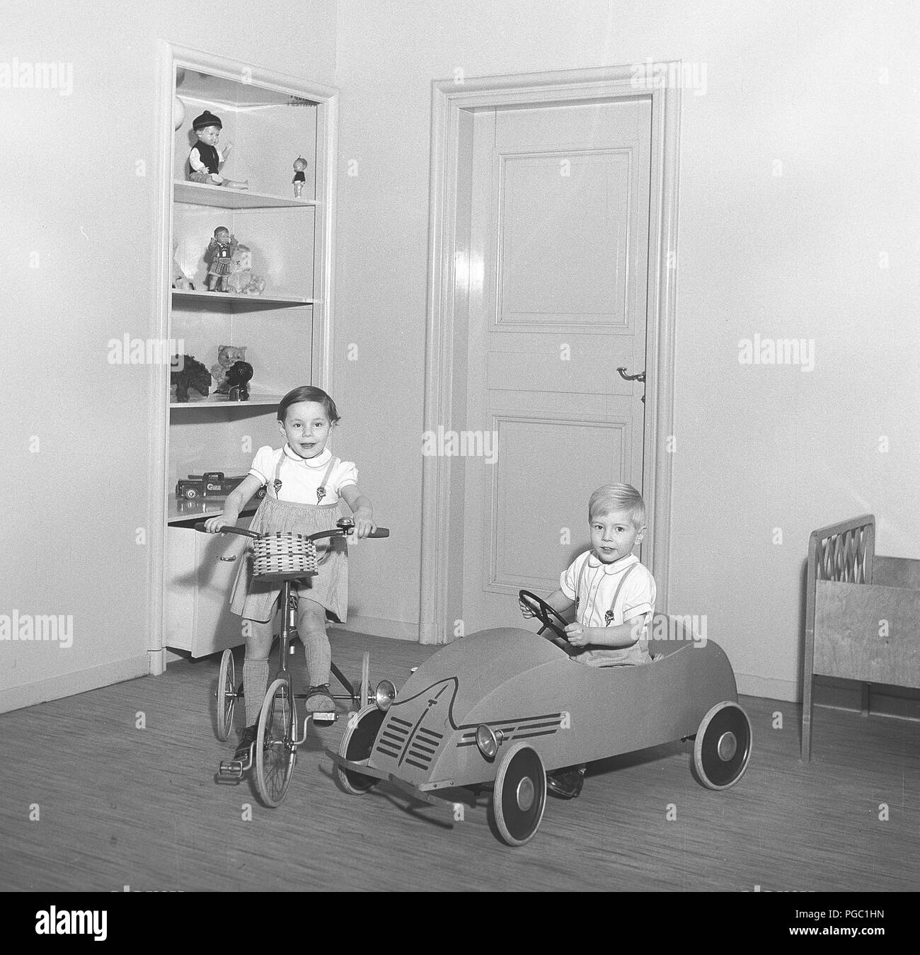 1950s children. Two children with their toys. The girls on her tricycle and the boy in his pedal car. Their toys are standing on the shelves behind.  Photo Kristoffersson ref CV23-3 Stock Photo