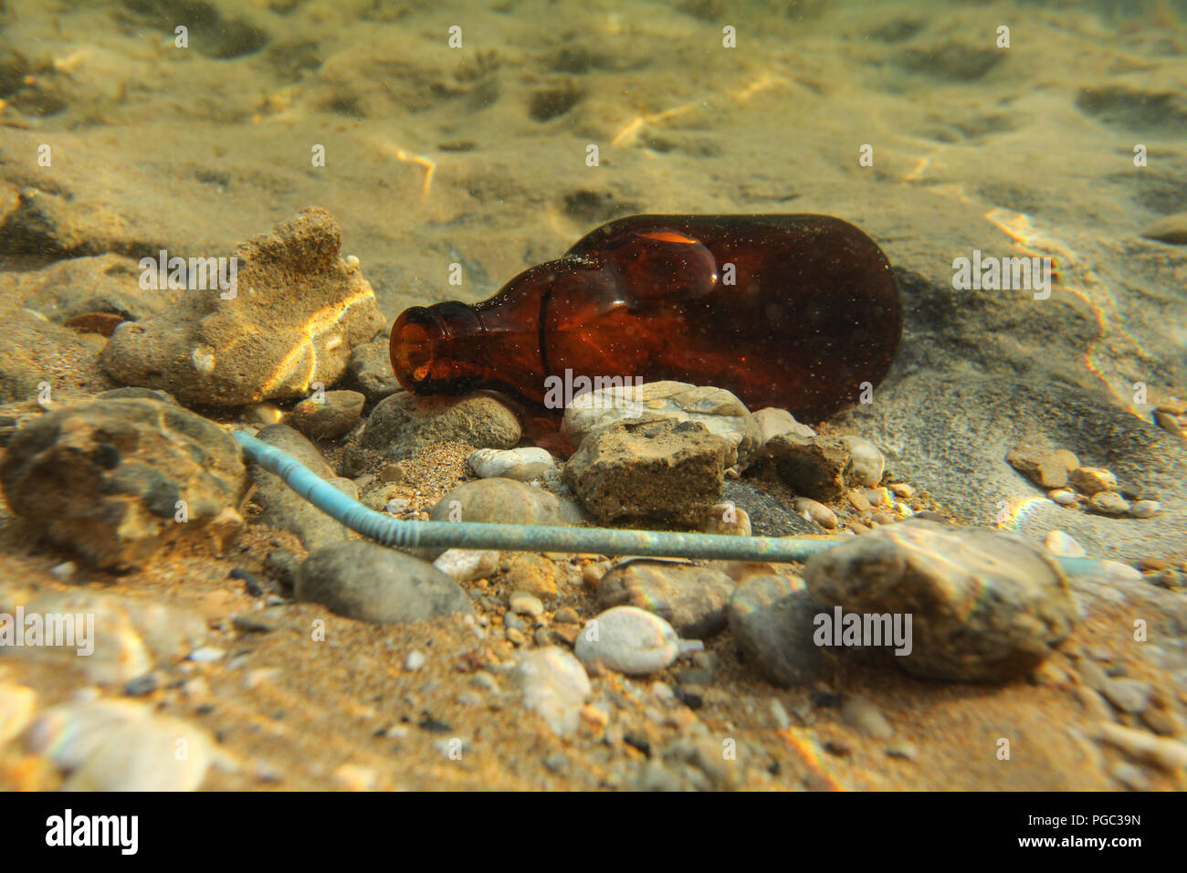 Beer bottle and plastic straw on sand sea bottom. Underwater photo, ocean littering / pollution concept. Stock Photo