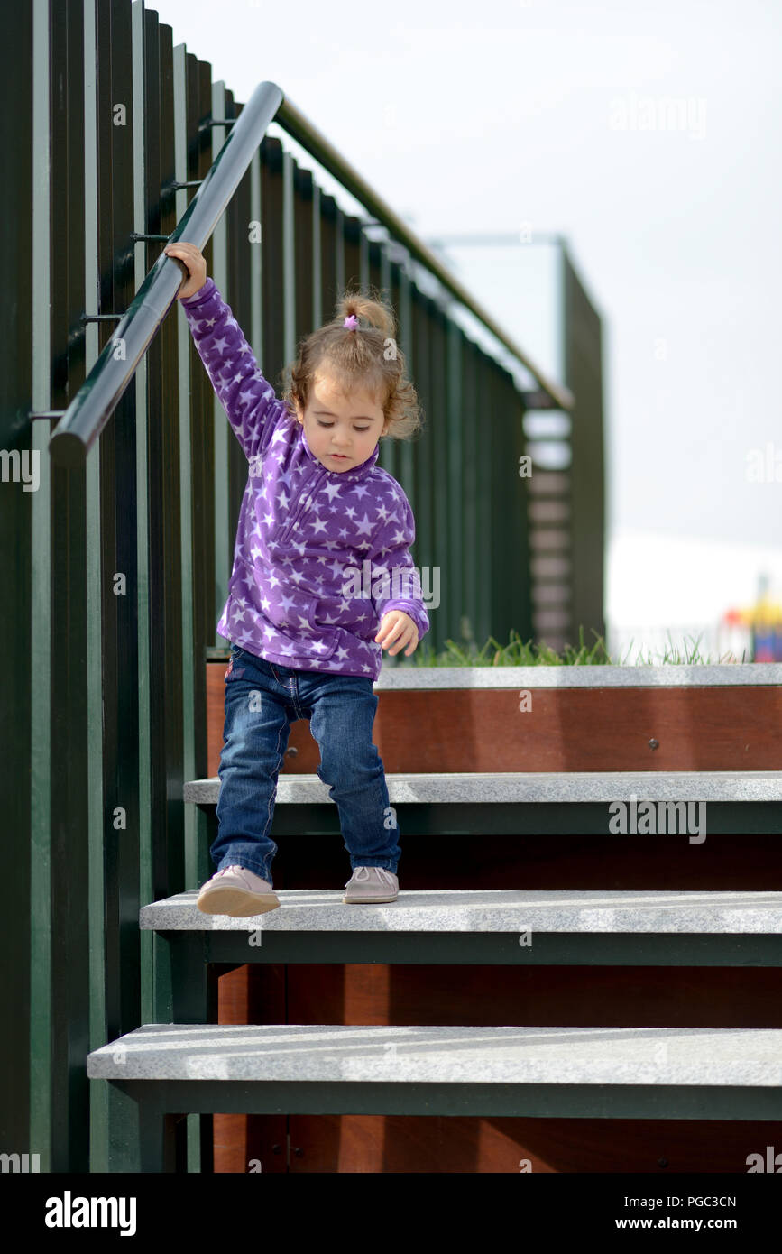 Little 20-month-old girl going down some stairs outdoors Stock Photo