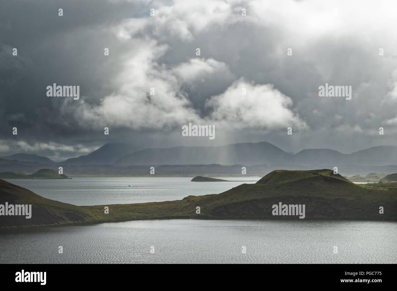 Large lake with islands, framed by mountains, individual areas are illuminated by the sun, in the background gray clouds and rain veils - Location: Ic Stock Photo