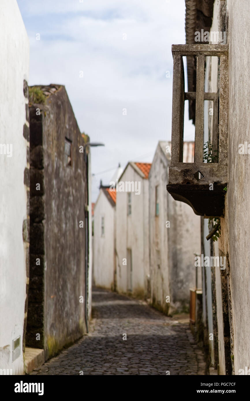 View into a paved arched alley with white and dark country houses, in the foreground a small balcony - Location: Azores, Corvo Island Stock Photo