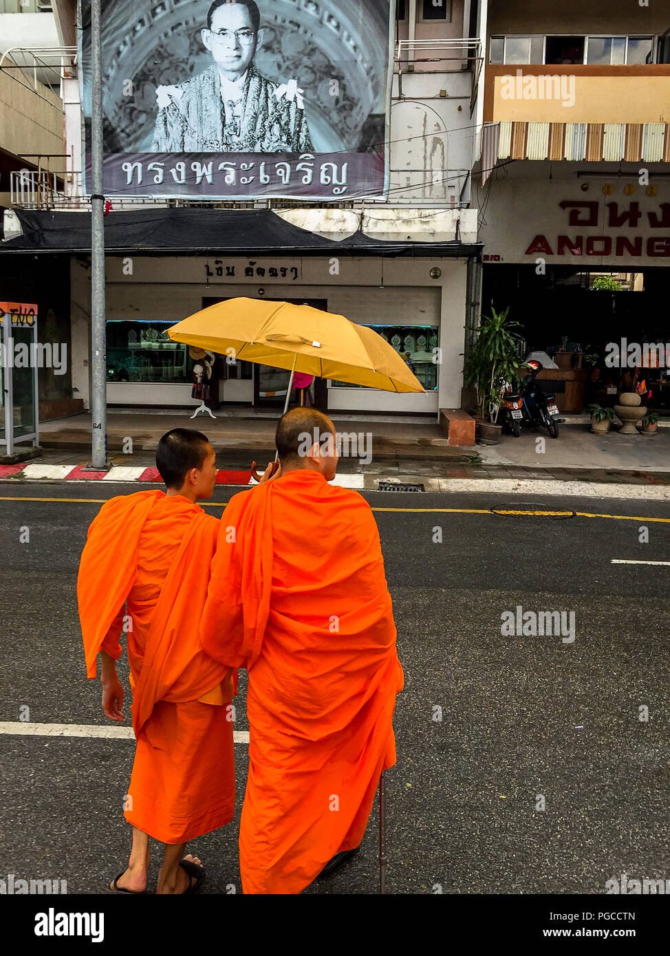 Two monks crossing the road with a poster of the King of Thailand over their heads in Chiang Mai. Stock Photo