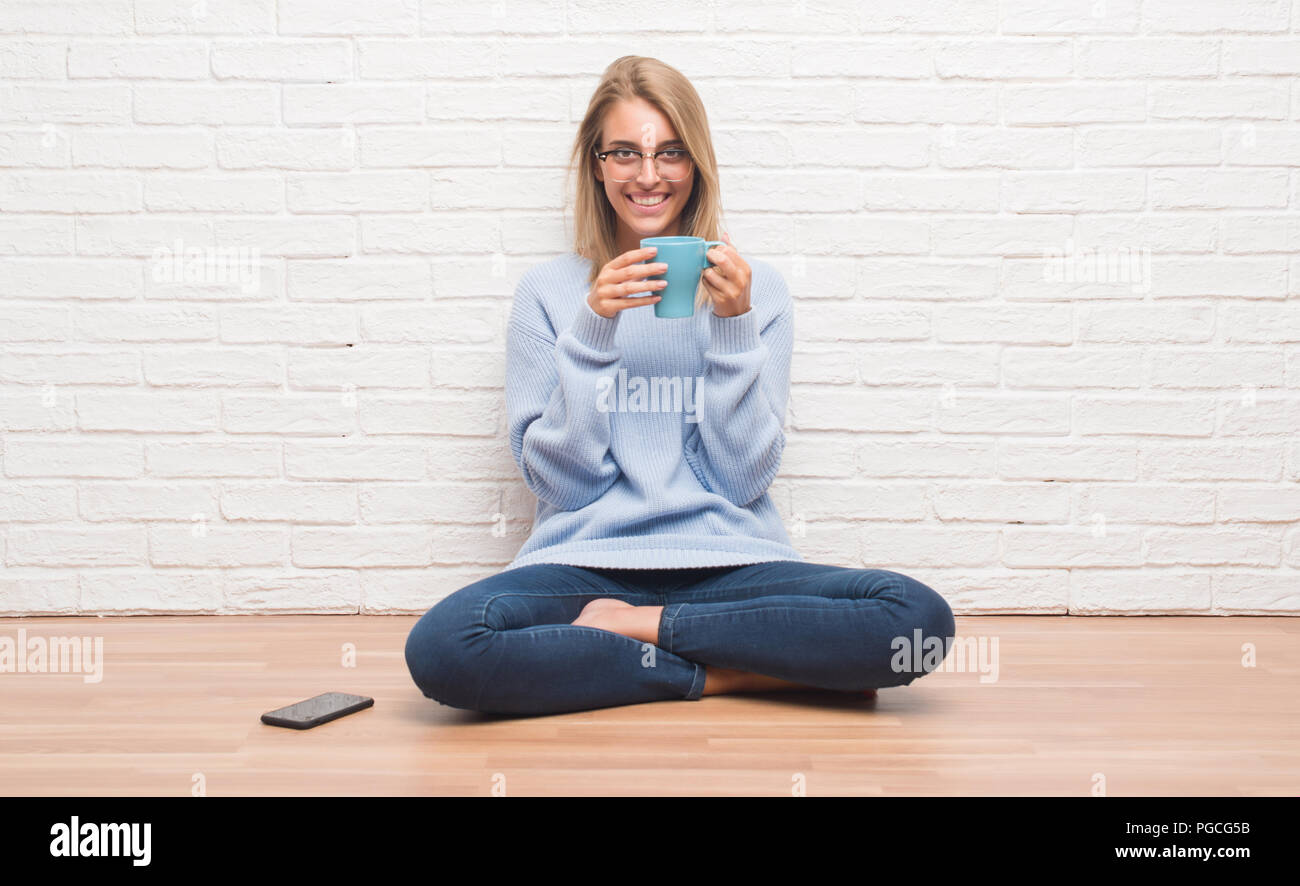 Beautiful young woman sitting on the floor driking cup of coffee at ...