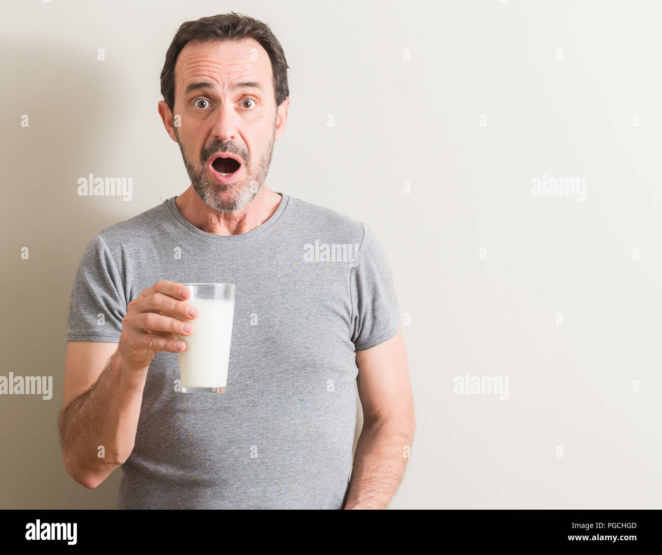 Senior man drinking a glass of milk scared in shock with a surprise ...