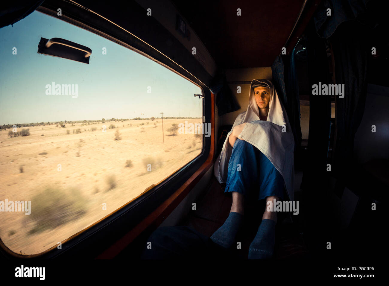 A young man on a lonely journey through the desert of Rajasthan, looks at the world from the train window. Stock Photo
