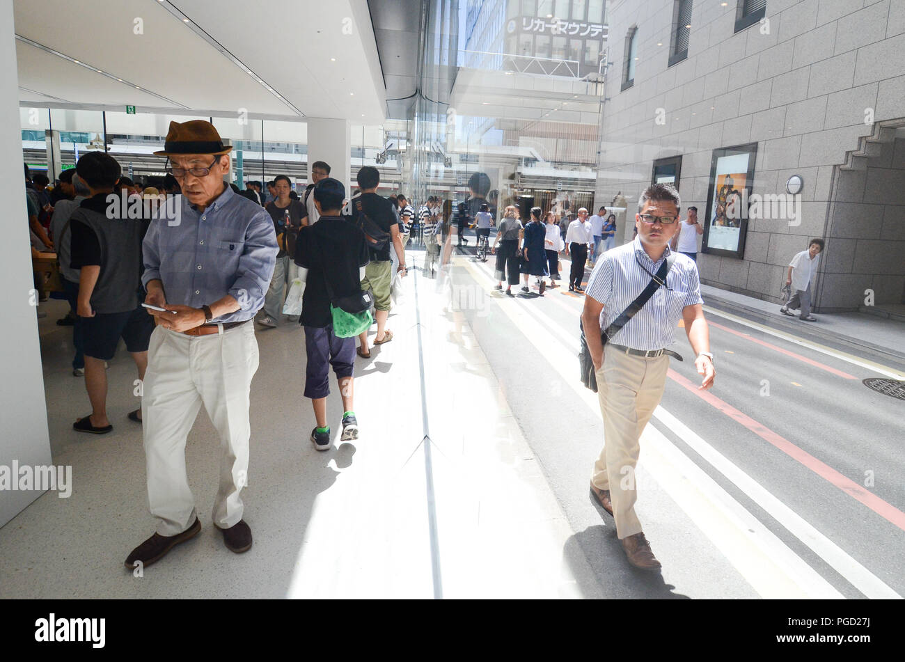 A pedestrian (right) walks peers into the Kyoto Apple Store from the street as he walks past the store on opening day — 25th August, 2018. Stock Photo