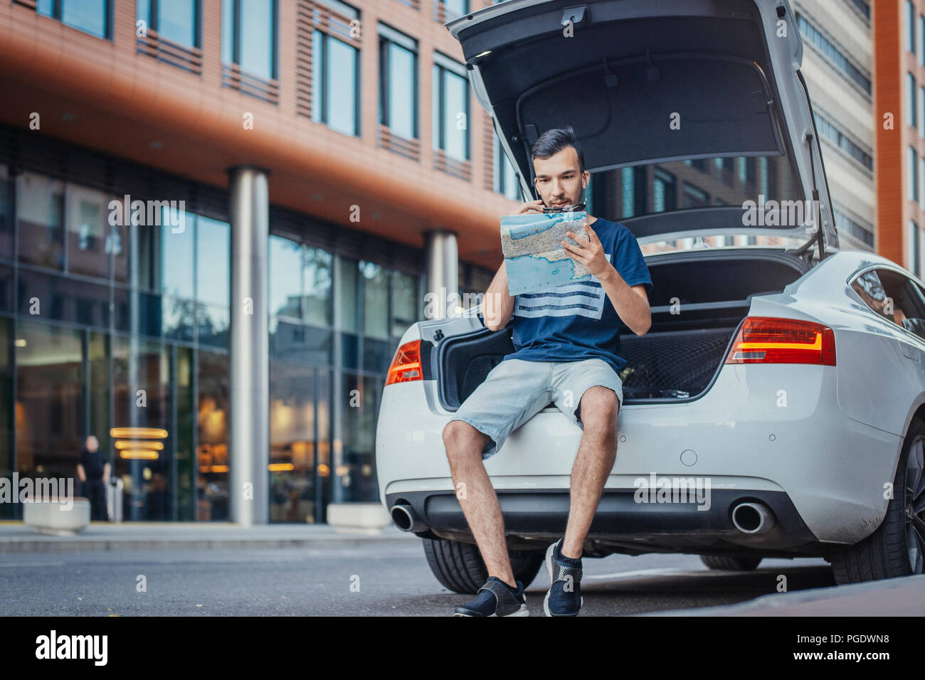 Distant plan of young man looking at map sitting in the truck of car. Man  and car are on focus and foreground, background blurred. Front view Stock  Photo - Alamy