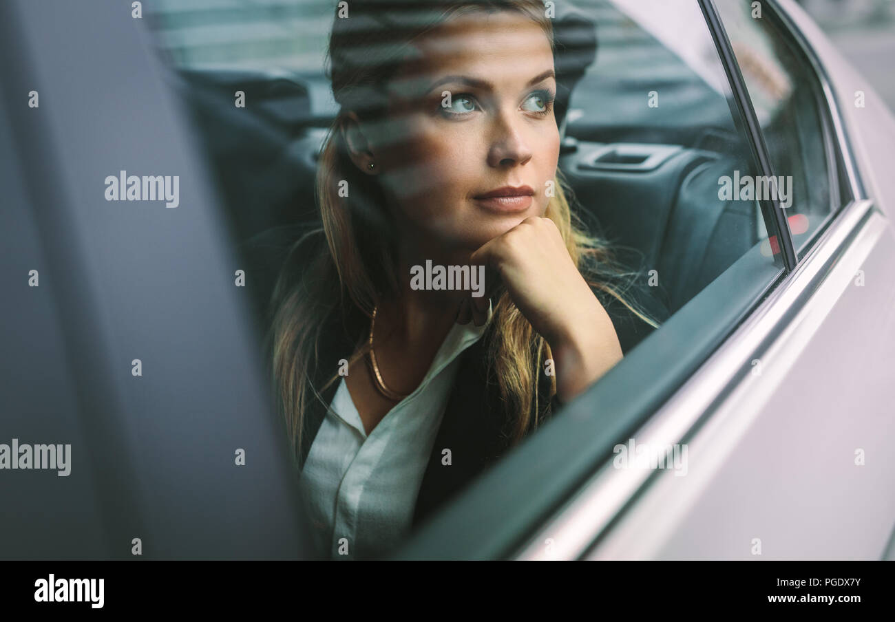 Beautiful young businesswoman sitting on back seat of a car and looking outside the window. Female business executive travelling by a cab. Stock Photo