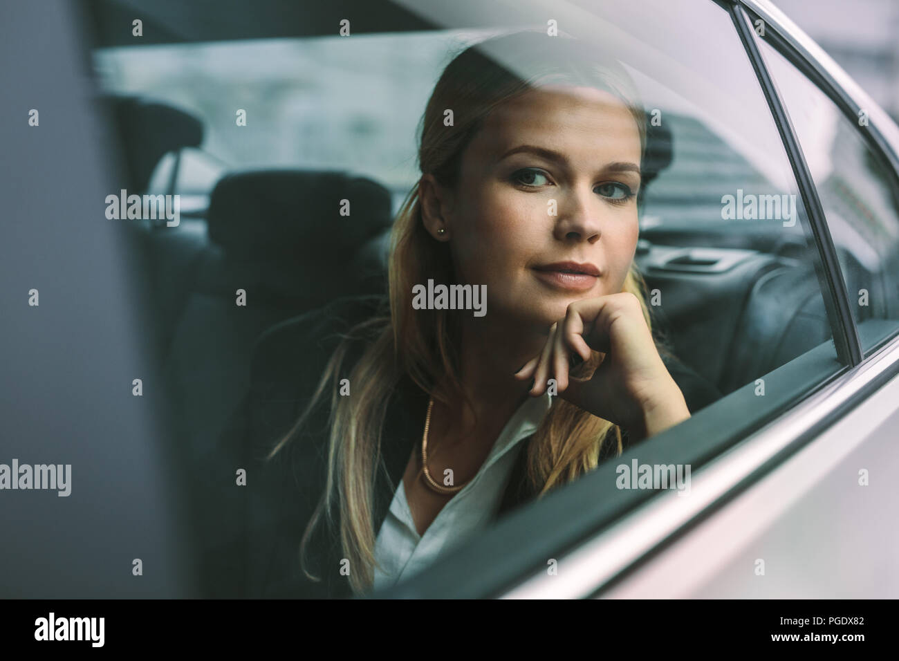 Confident young businesswoman sitting on back seat of a taxi and looking outside the window. Female executive travelling by a car. Stock Photo