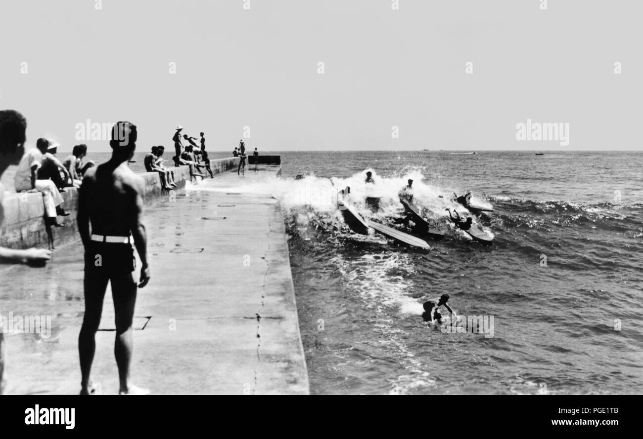 California surfers catching a wave along the Newport Harbor jetty in Corona del Mar in the early 1930s. This famous spot in surfing history was home of the Corona del Mar Surfboard Club, formed in 1928 with members including Hawaii's Duke Kahanamoku, Redondo's Tom Blake, Gene 'Tarzan' Smith, and Gerard and Art Vultee of the Los Angeles Athletic Club. It was also the site of one of the first surfing championships on the US mainland, the Pacific Coast Surfboard Championship, which began in 1928. Stock Photo