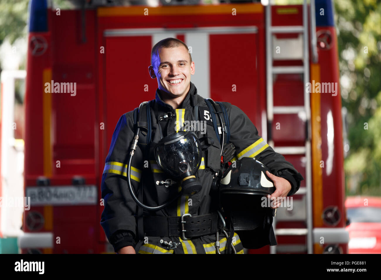 Photo of happy fireman with gas mask and helmet near fire engine Stock Photo