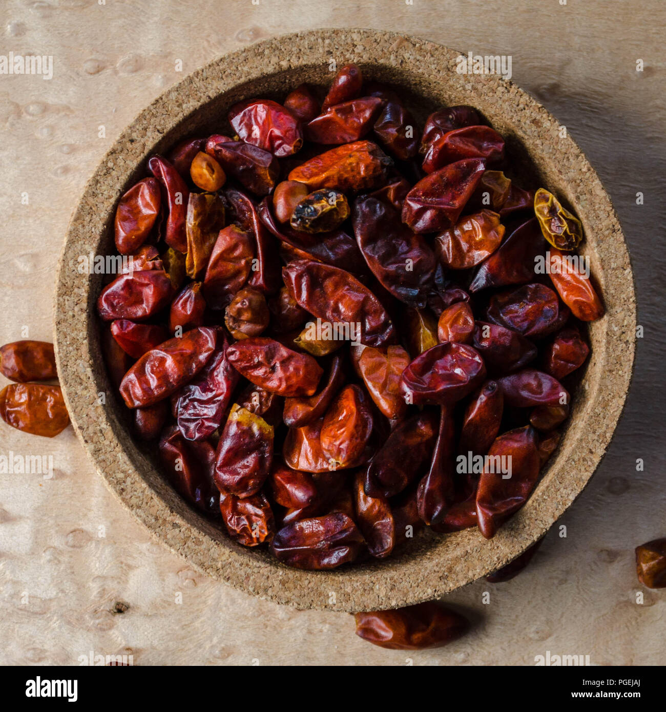 Pequin chilies in a small cork bowl against a birdseye maple background, shot flat-lay (Capsicum annuum var. glabriusculum) Stock Photo