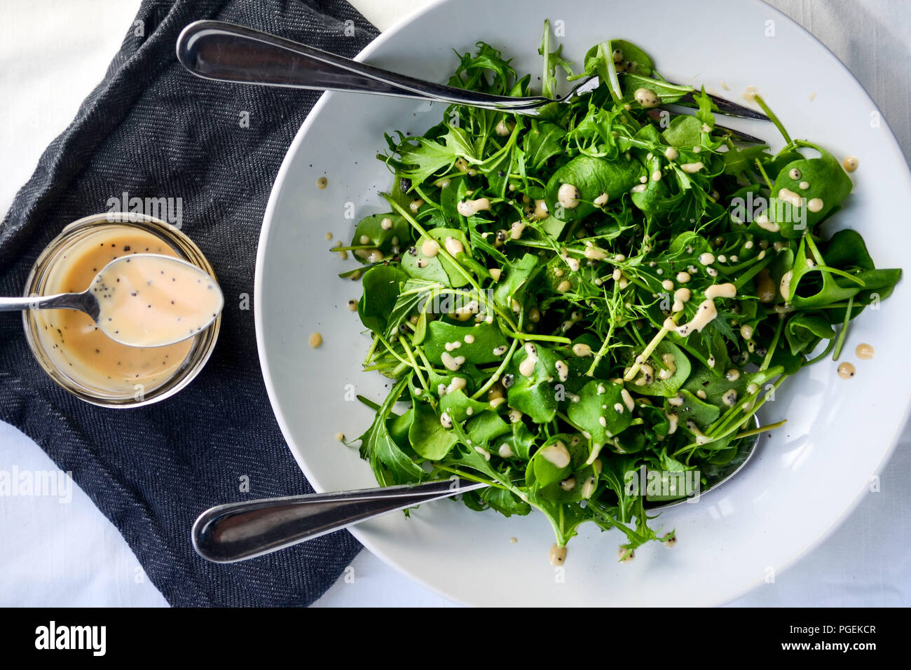Flat-lay green salad of mizuna and miner's lettuce served with a rhubarb and poppy seed vinaigrette, served in a white bowl with two serving spoons. Stock Photo