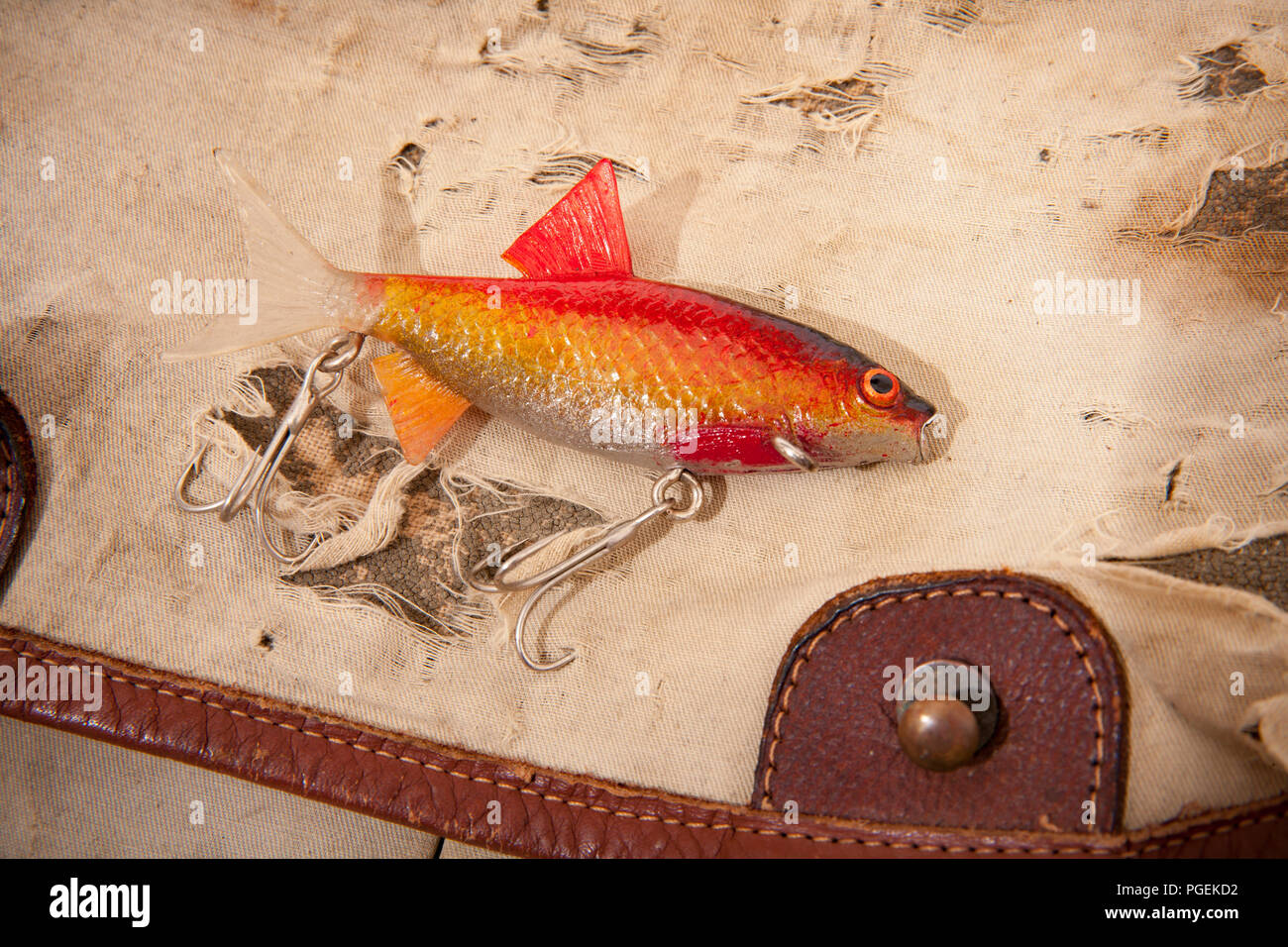 A lifelike plastic fishing lure with treble hooks displayed on an old fishing tackle bag. From a collection of vintage fishing tackle. North Dorset En Stock Photo