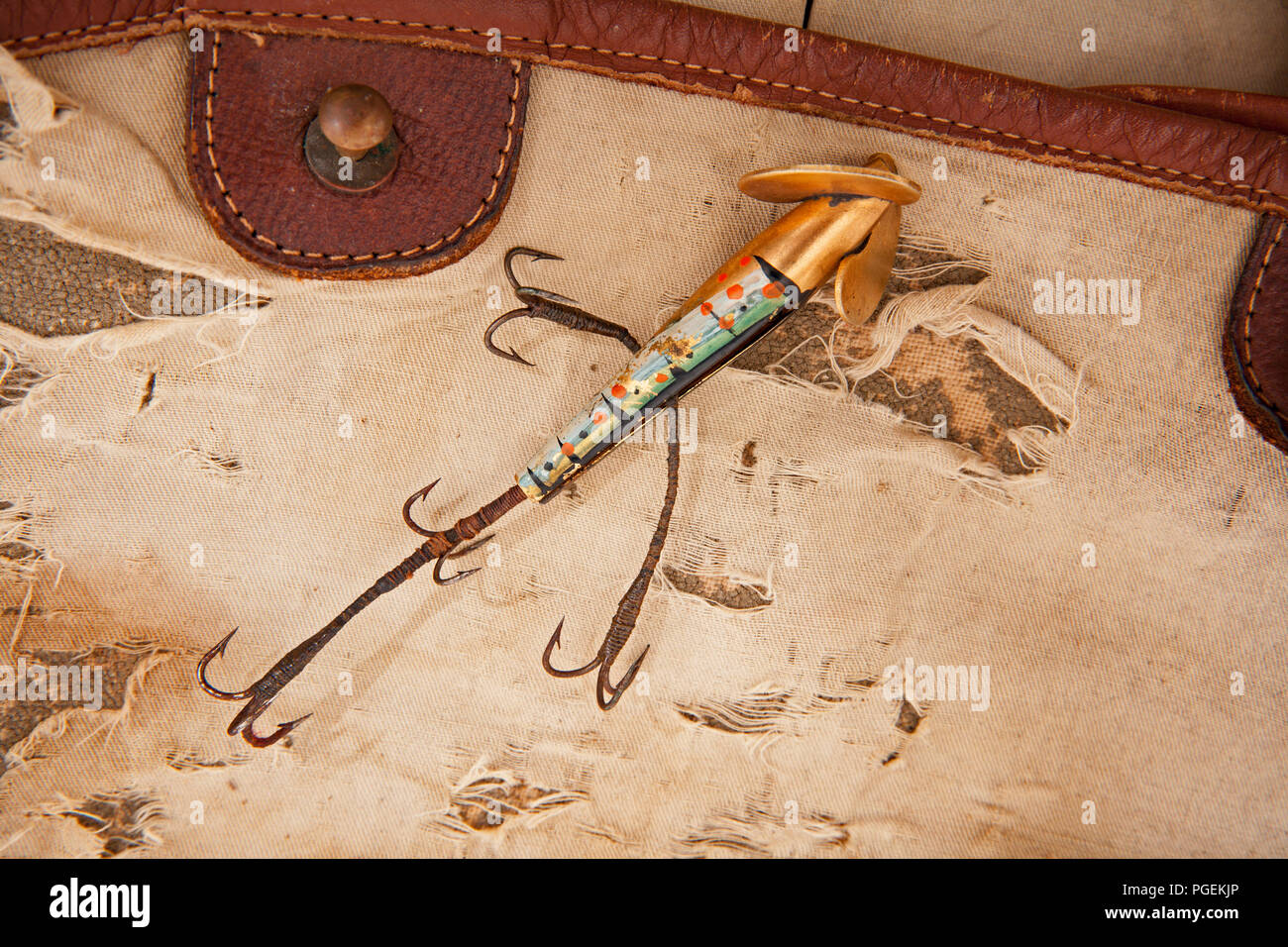 An old metal Foster’s Kill Devil fishing lure equipped with four treble hooks and displayed on an old fishing tackle bag. From a collection of vintage Stock Photo