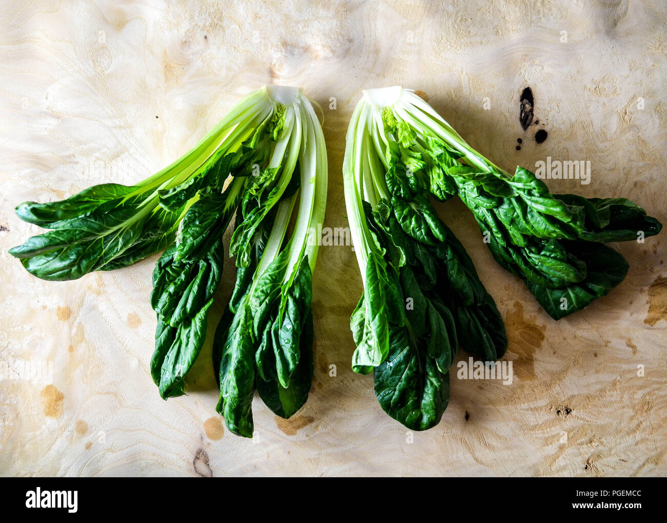 A head of tatsoi (Brassica rapa subsp. narinosa), aka rosette bok choy or spoon mustard, shown in cross-section against a burl-wood background. Stock Photo